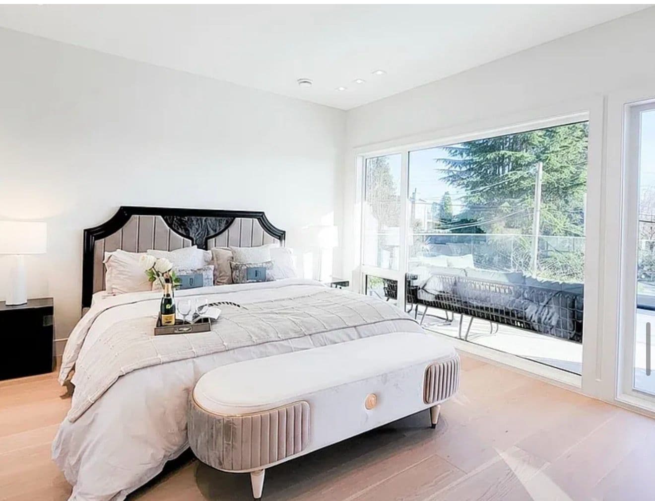 Luxury staged primary bedroom with an upholstered headboard and a private balcony view